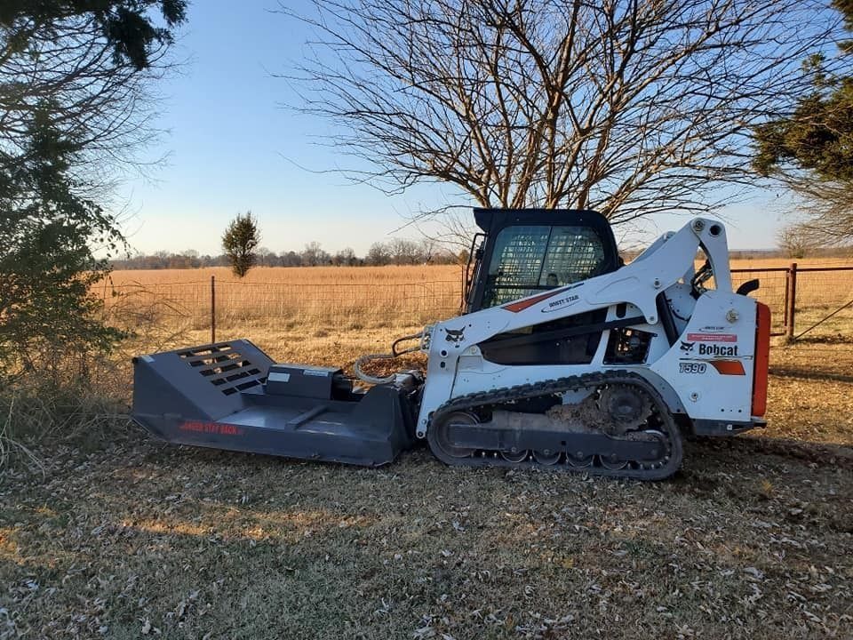 White skid steer with brush mower attachment clearing brush in a field near trees