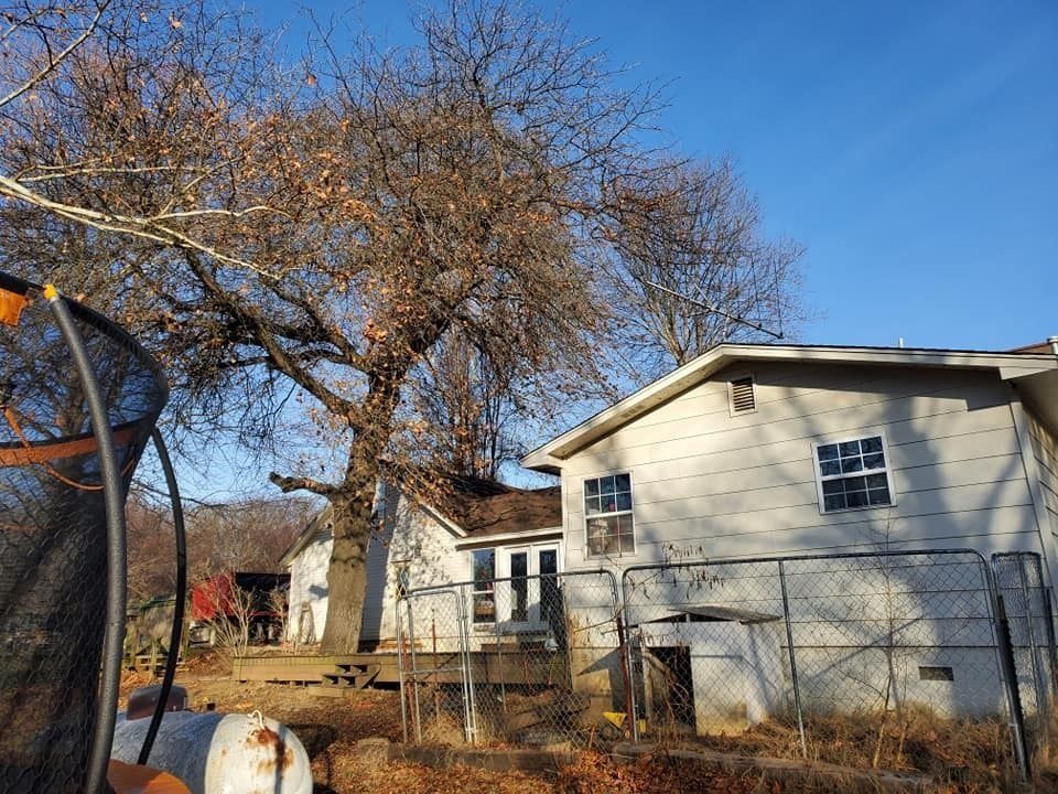 Suburban house with bare trees and a chain-link fence under a clear blue sky