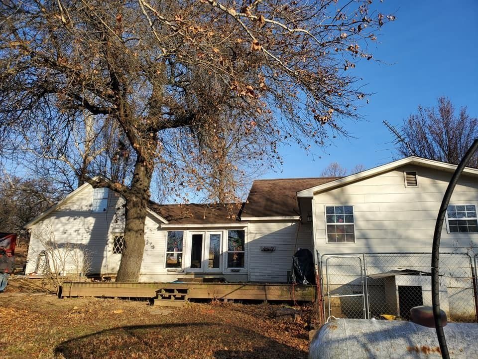 Suburban house with white siding, large bare tree, and a clear blue sky in autumn.