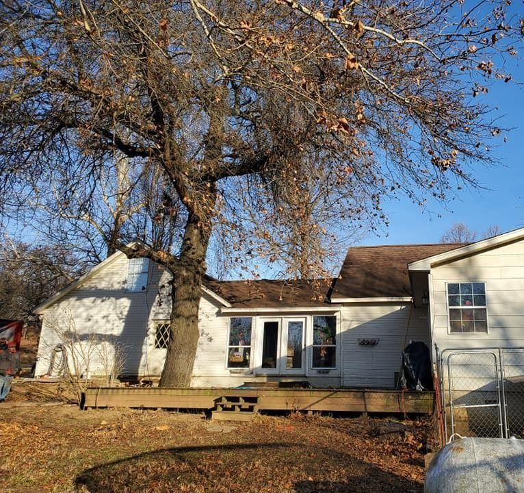 White house with a deck and large bare trees in a yard on a sunny day
