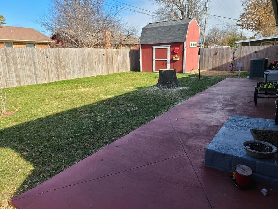 Backyard with red shed, fenced lawn, and concrete patio on a sunny day