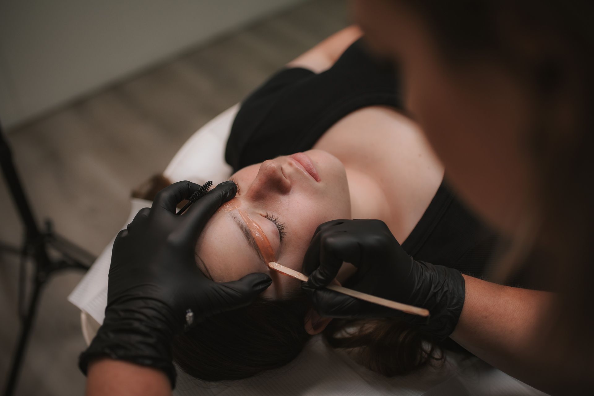 Person receiving eyebrow waxing, performed by gloved hands.