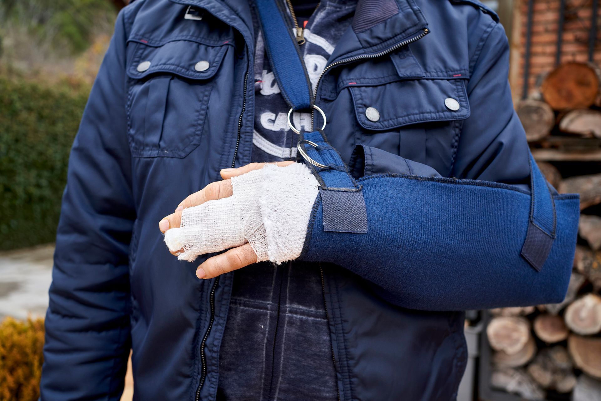 Man wearing a blue sling and bandage on his hand, possibly from an injury. He is standing outdoors.
