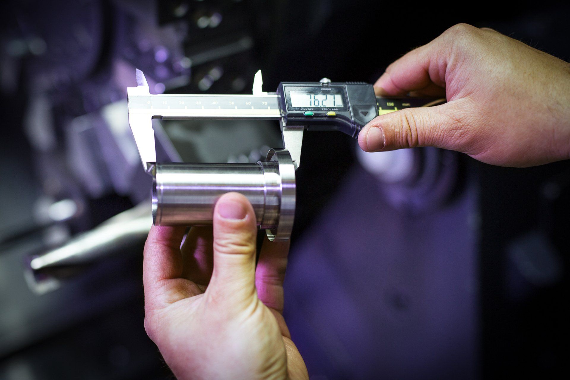 A person is measuring a piece of metal with a digital caliper.