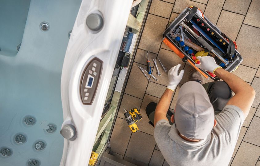A person in a gray cap is fixing a hot tub with a toolbox.