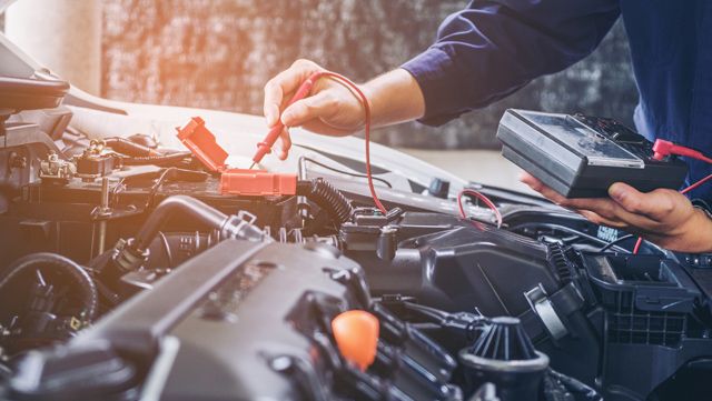 Un mécanicien travaille sur un moteur de voiture avec un multimètre.