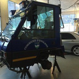 Un véhicule bleu est garé dans un garage à côté d'une voiture argentée.
