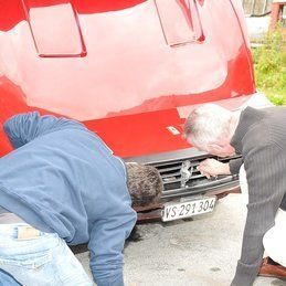 Deux hommes regardent sous le capot d'une voiture rouge.
