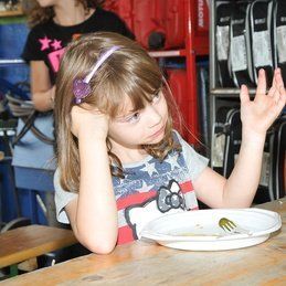Une petite fille est assise à une table avec une assiette de nourriture.