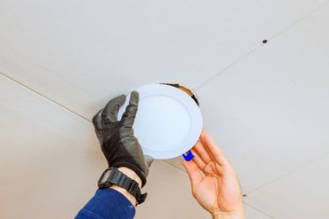 Mit Handschuhen wird eine Einbauleuchte in eine weiße Deckenplatte montiert.