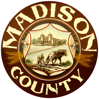 Madison County seal, brown and gold. Includes a shield with a building and farmers plowing a field.