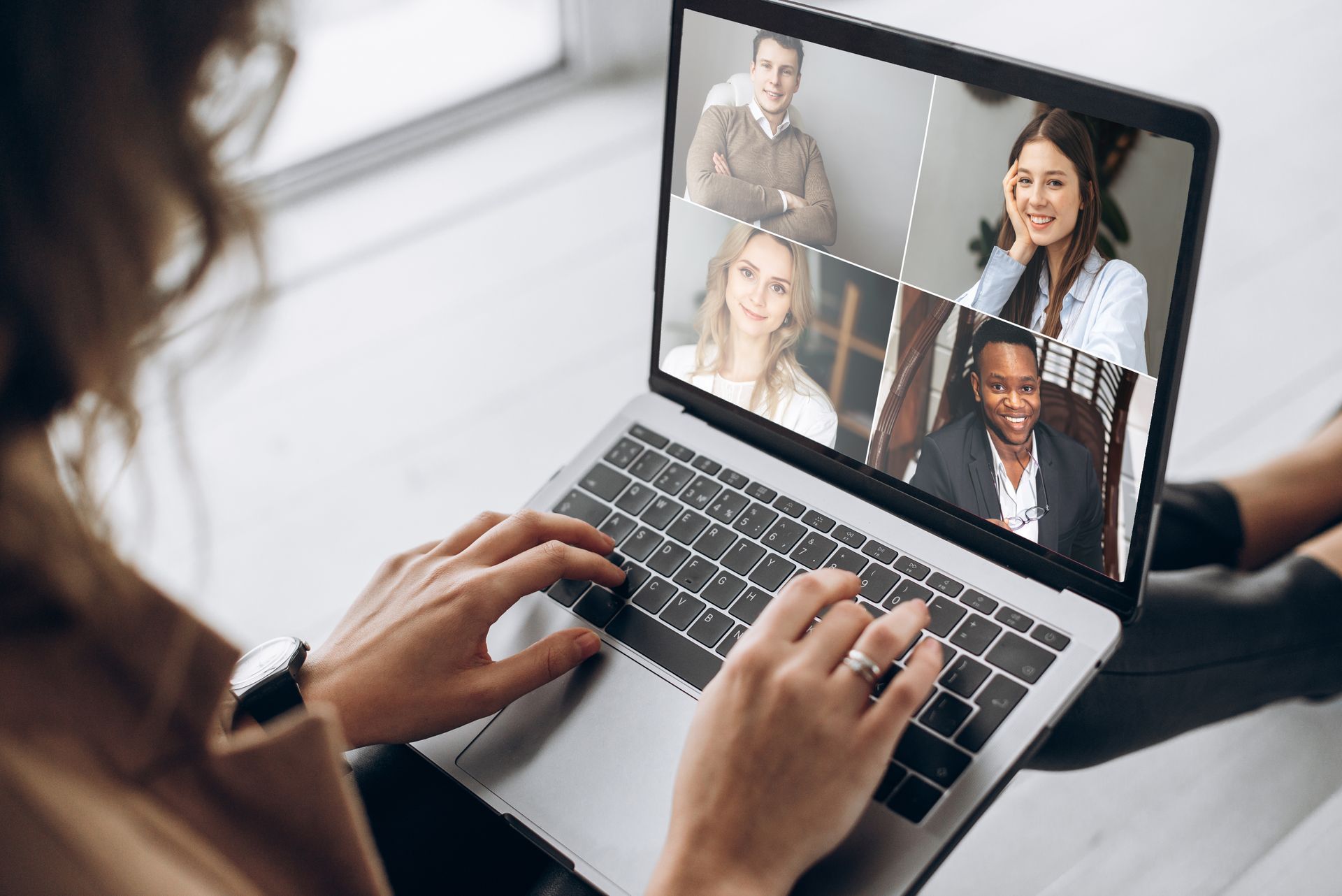 Person using laptop, in a video call with four other people; screen shows video feeds.