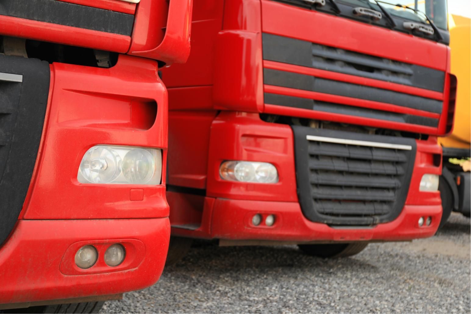 Two red semi-trucks parked side by side, shown from the front on gravel.