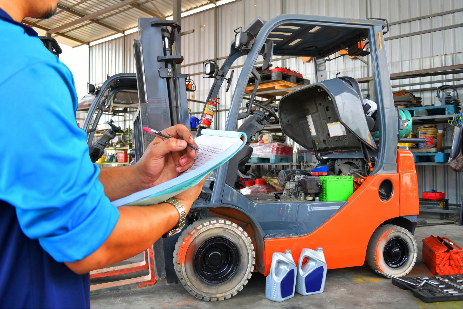 Worker writing on a clipboard beside an orange forklift in a workshop