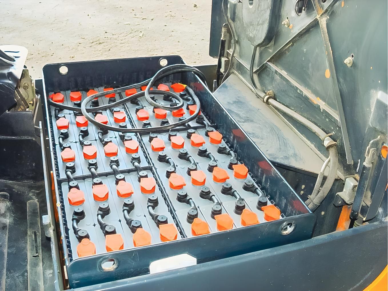 Open battery compartment with rows of orange-topped batteries and connecting cables