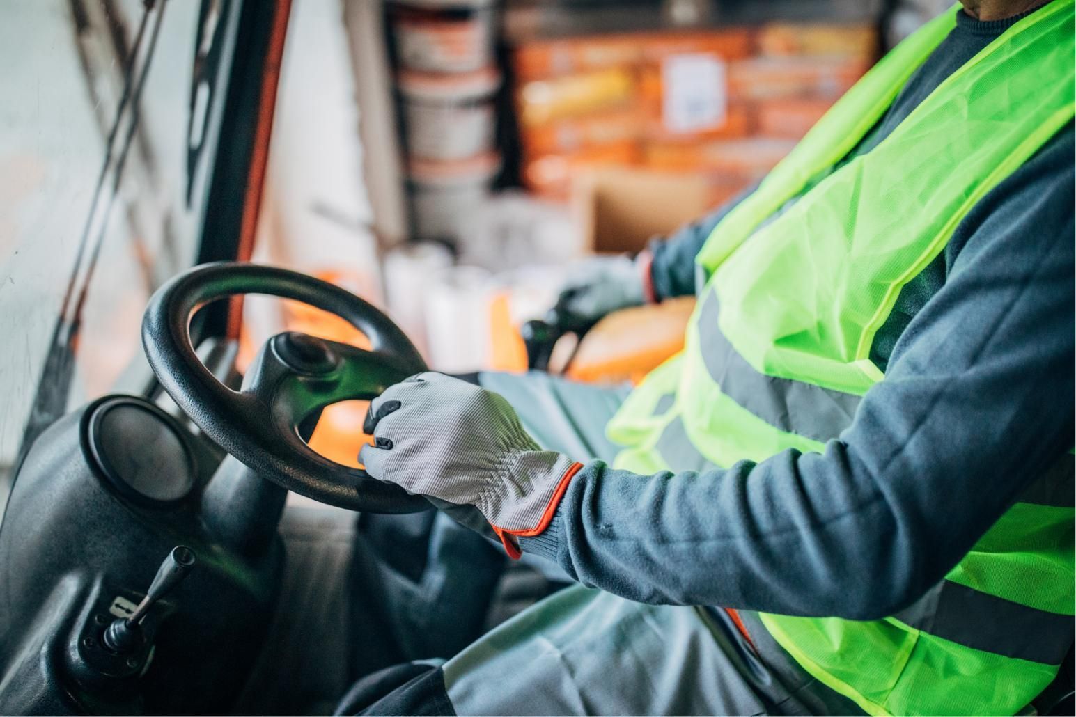 Driver in neon safety vest steering a vehicle, hands on the wheel inside a work truck cabin