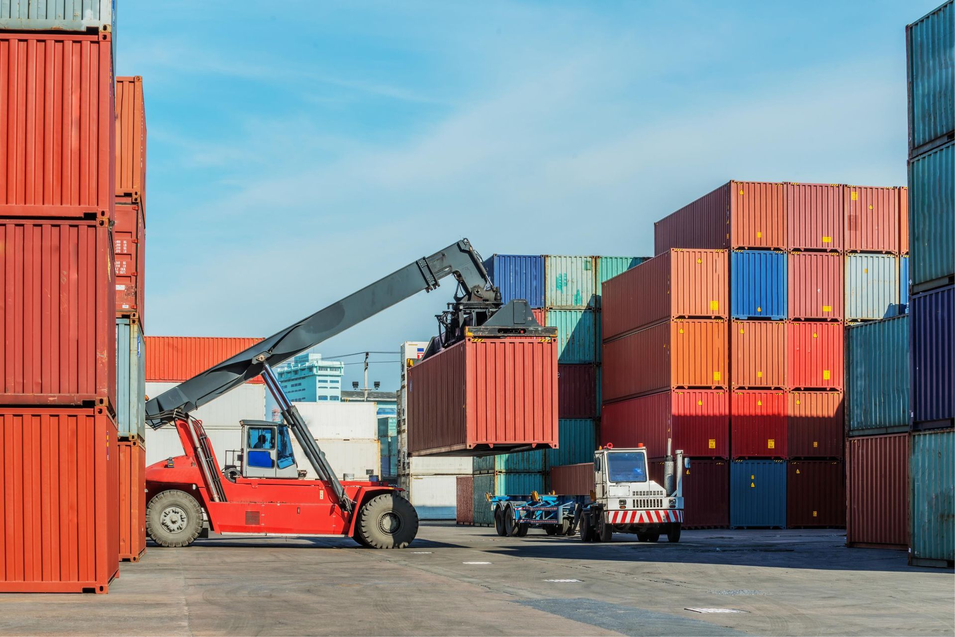 Forklift moving shipping containers in a cargo yard under a blue sky
