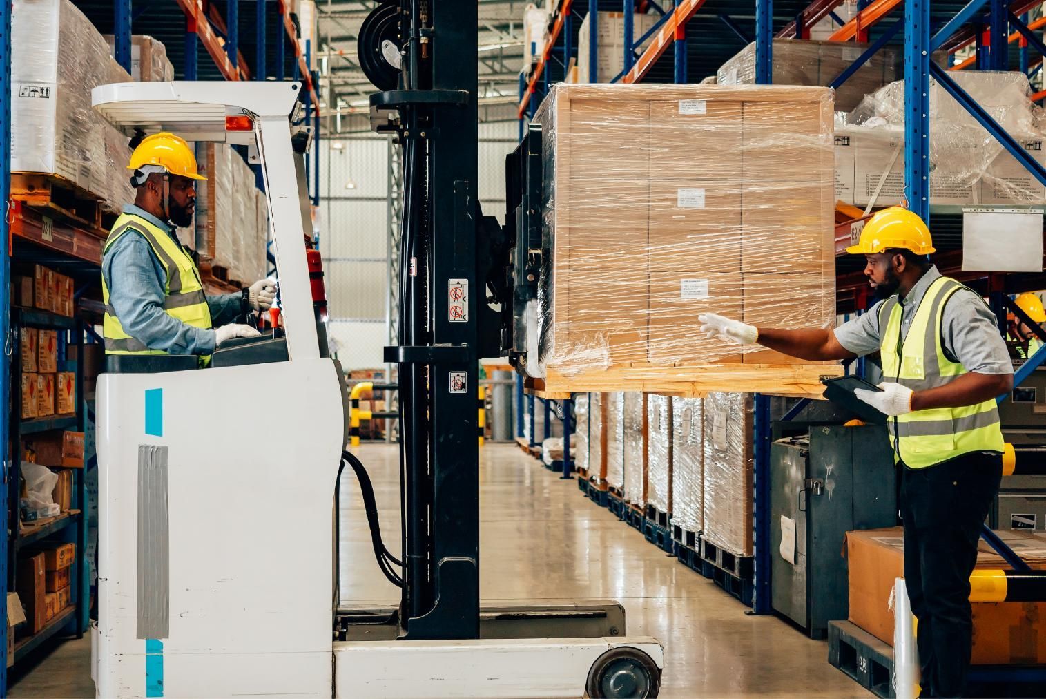 Warehouse workers moving a shrink-wrapped pallet with a forklift in an aisle of stacked shelves