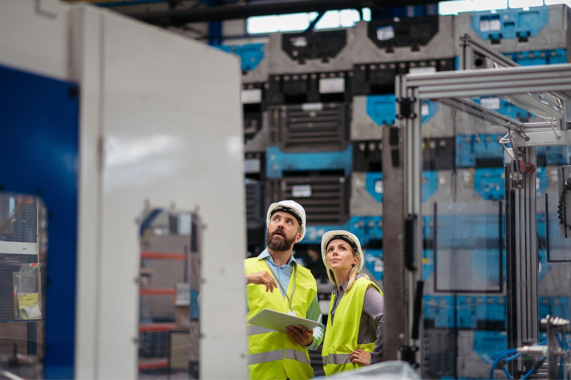 Two workers in yellow safety vests inspecting industrial equipment in a factory aisle