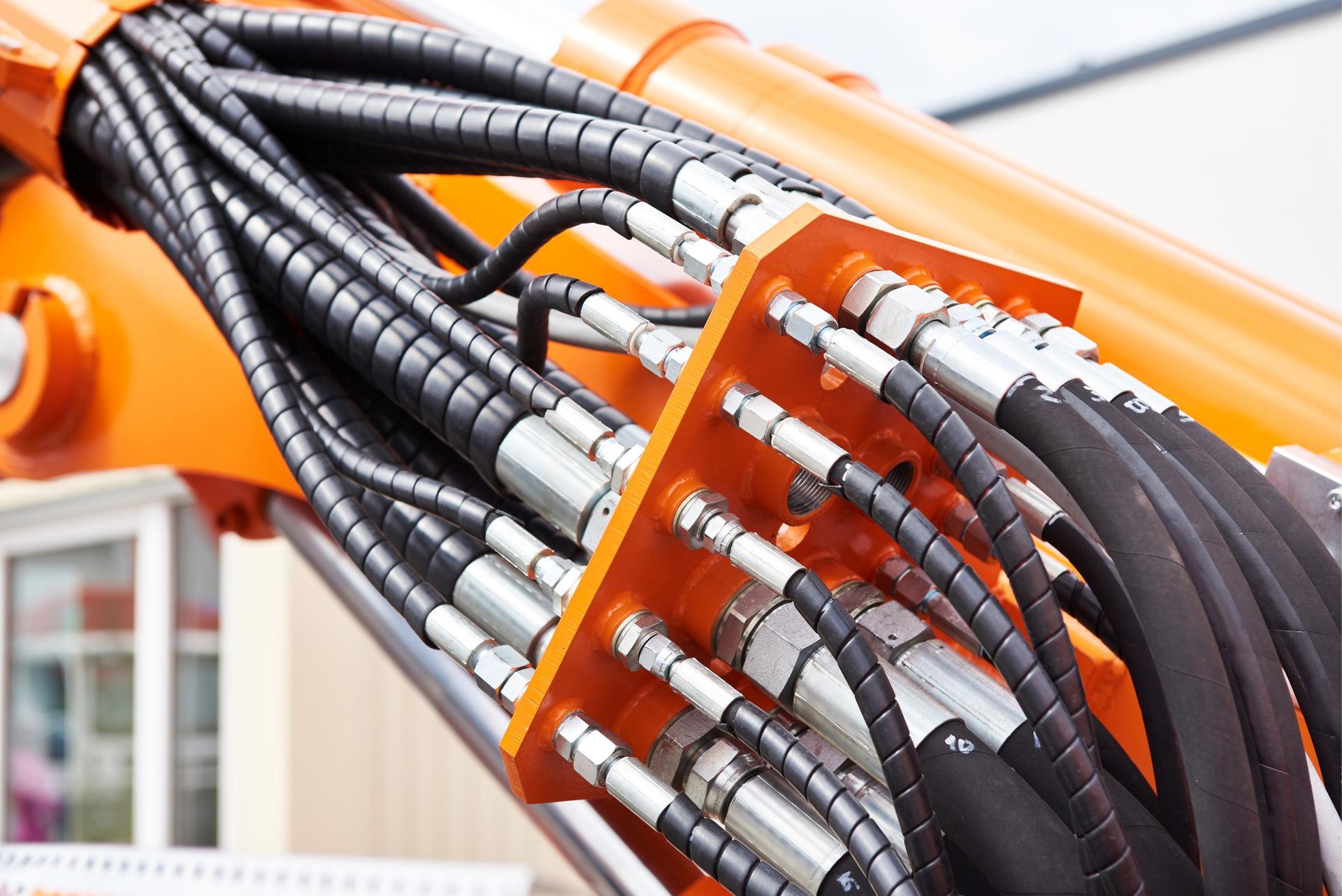 Close-up of orange industrial machinery with bundled black hydraulic hoses and silver fittings