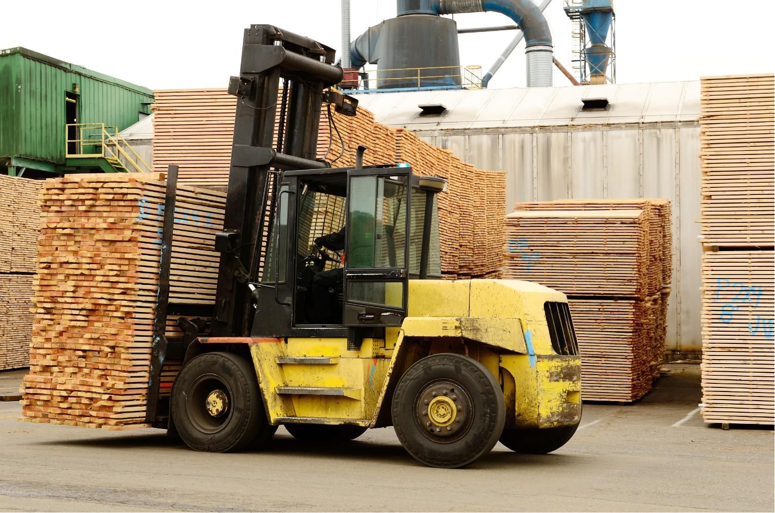 Yellow forklift carrying lumber stacks in an industrial yard