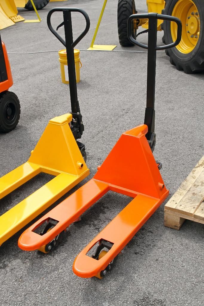 Two pallet jacks, one yellow and one orange, on pavement near a wooden pallet.