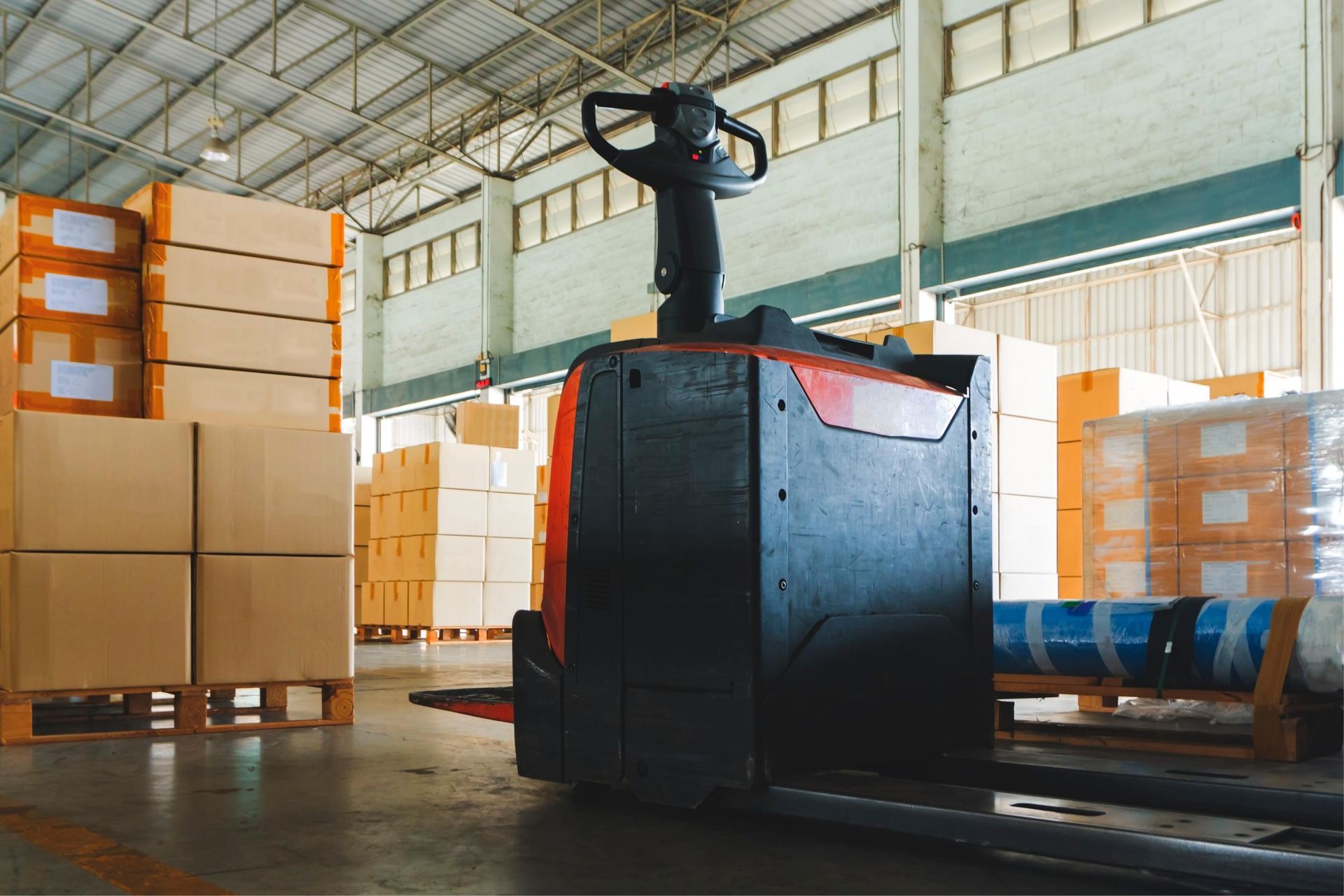 Forklift in a warehouse aisle beside stacked boxes and wrapped pallets