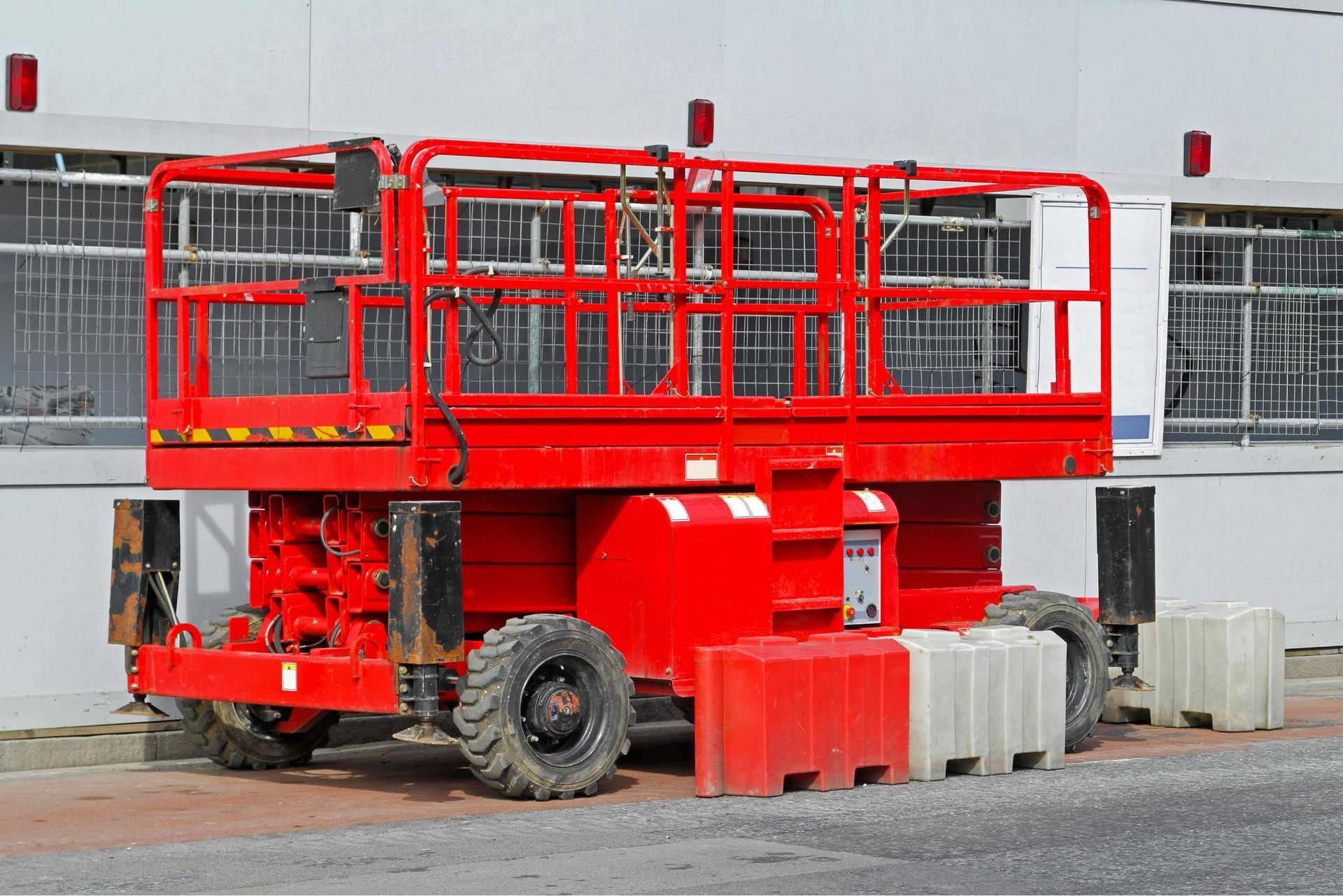 Red construction lift with railings parked beside a building