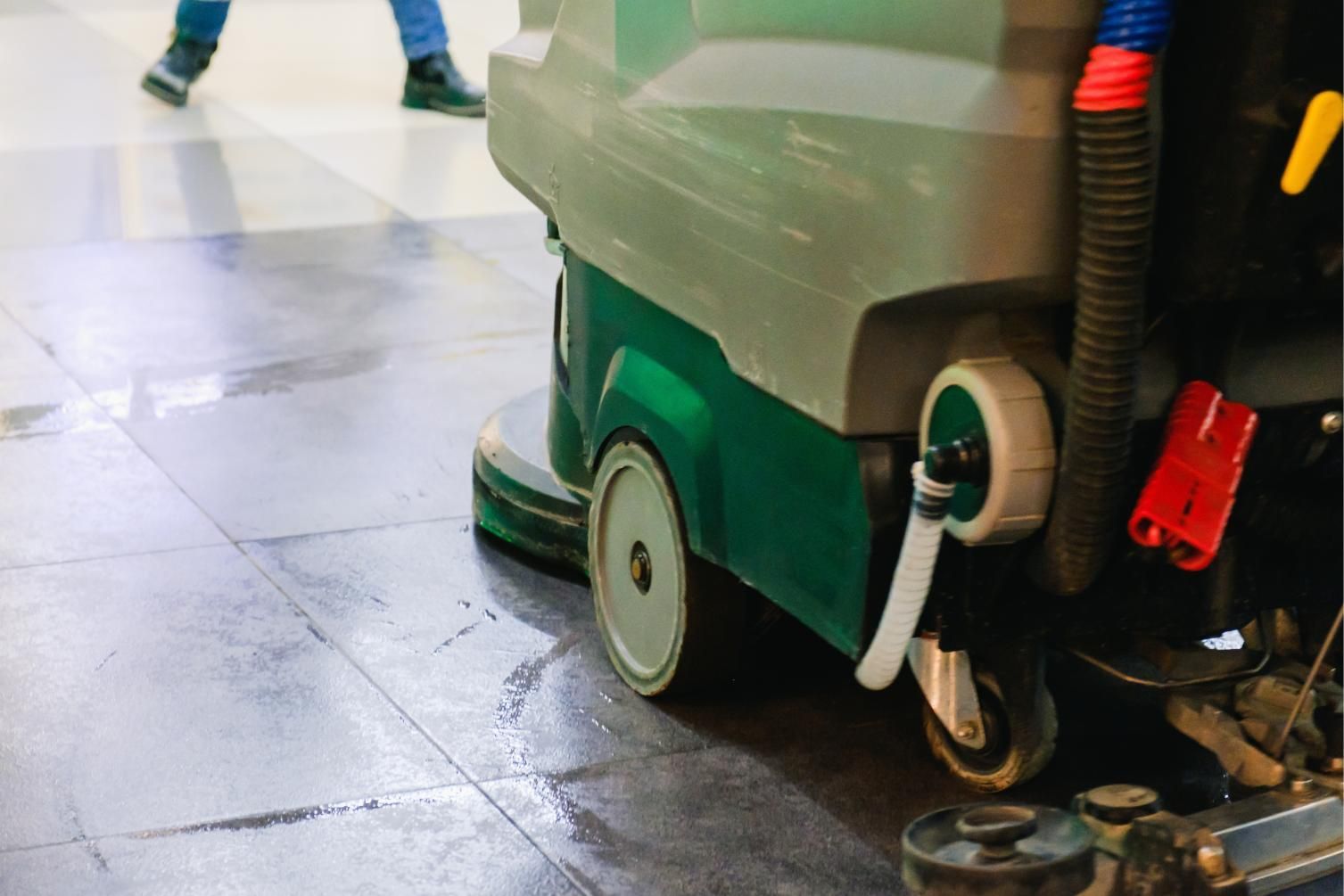 Floor scrubber machine cleaning a shiny tiled floor in an indoor space