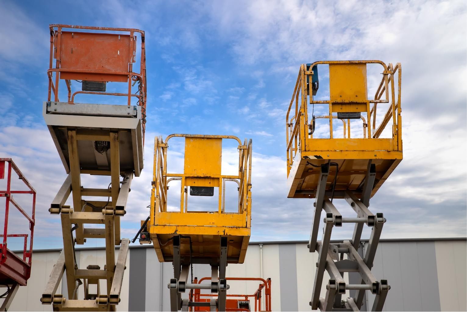 Three elevated work platforms in orange and yellow against a blue sky