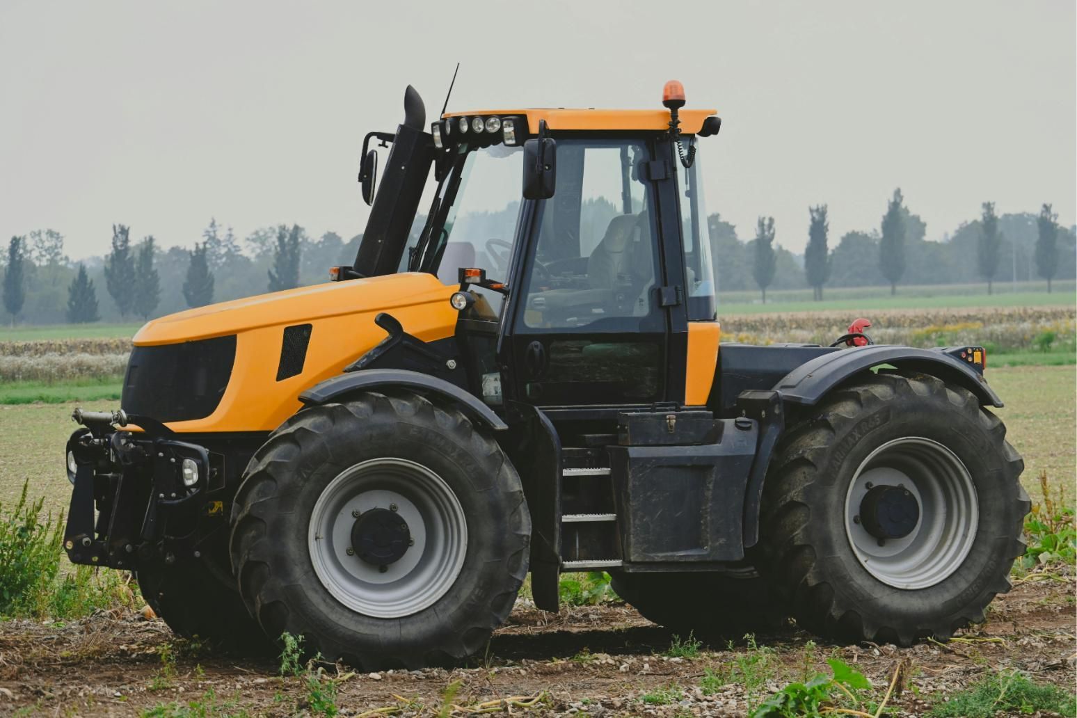 Yellow-and-black tractor in a field, viewed from the side, with large tires and a cab.