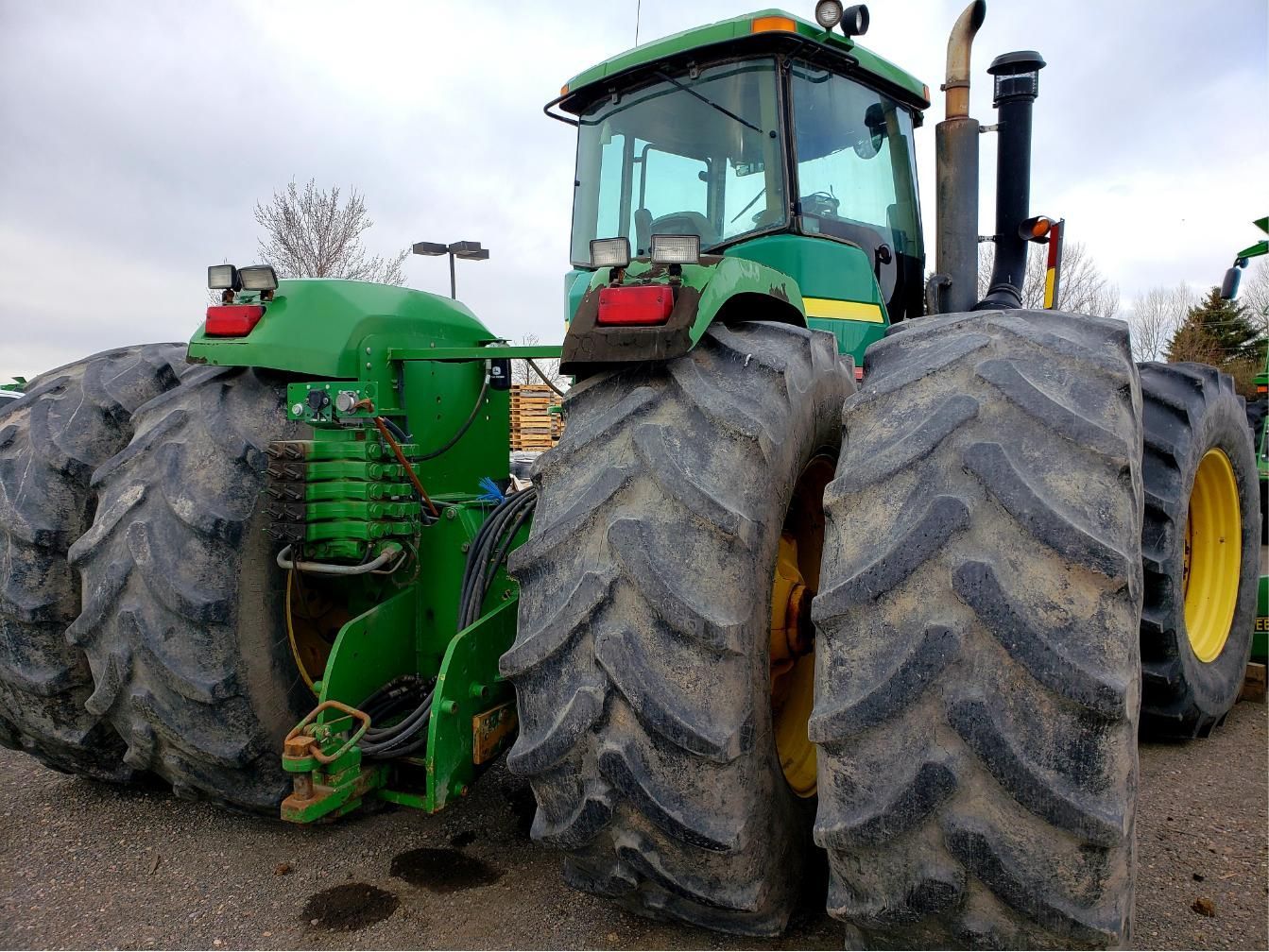 Large green agricultural tractor with oversized muddy tires parked outdoors in a field.