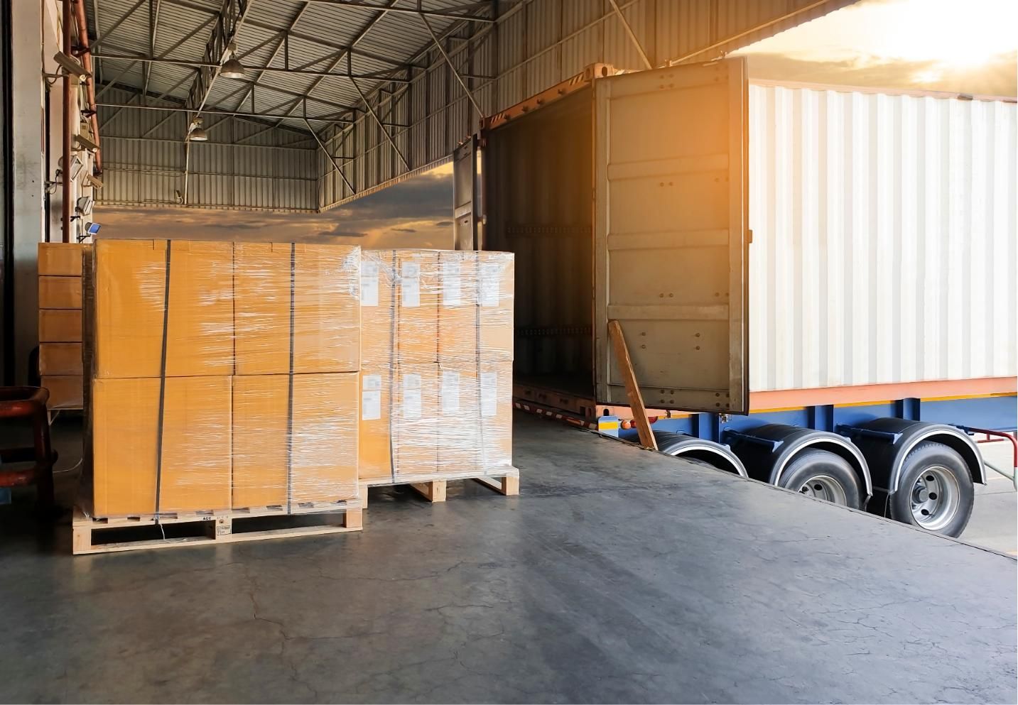 Warehouse with stacked palletized boxes and a truck trailer being loaded at the dock.