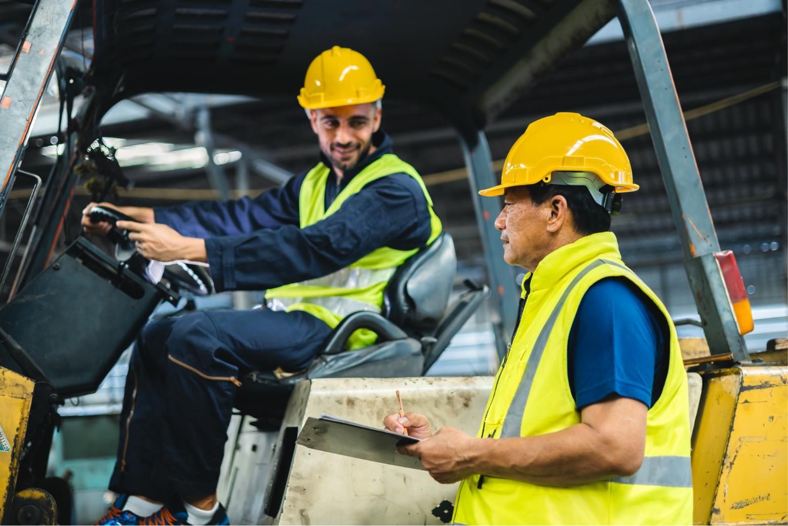 Two workers in yellow hard hats and safety vests operating heavy machinery in an industrial setting