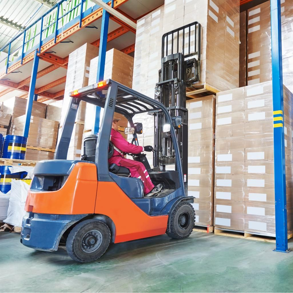 Forklift operator in pink jacket moving pallets in a warehouse aisle
