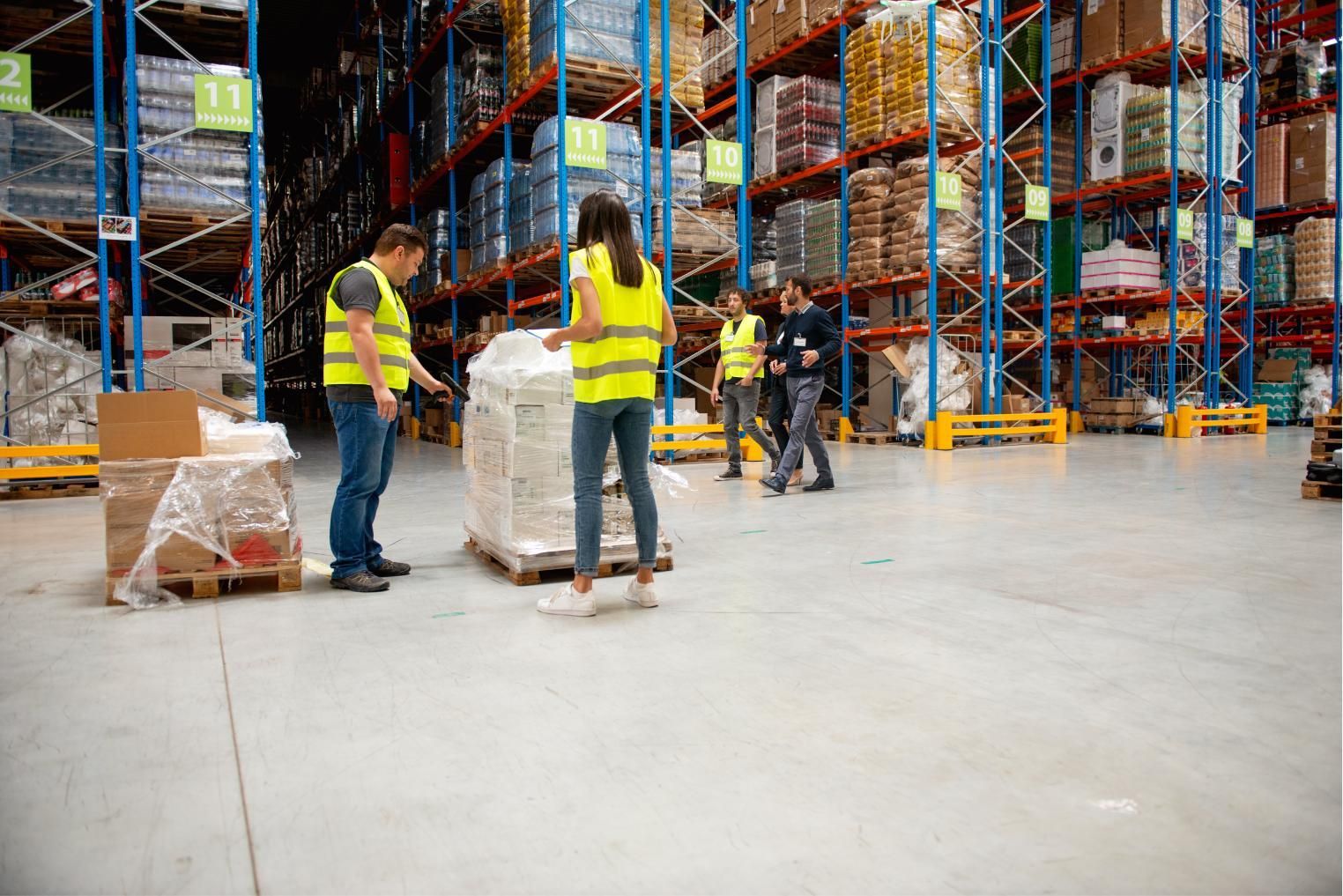 Workers in yellow safety vests moving pallets in a warehouse aisle