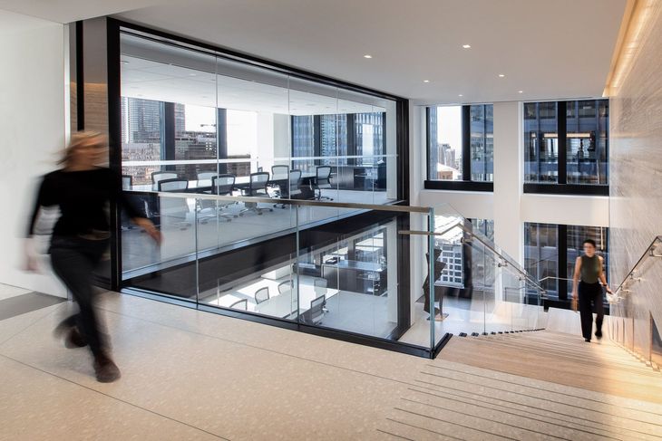 Modern office stairwell with glass walls, blurred person walking, and city views through large windows