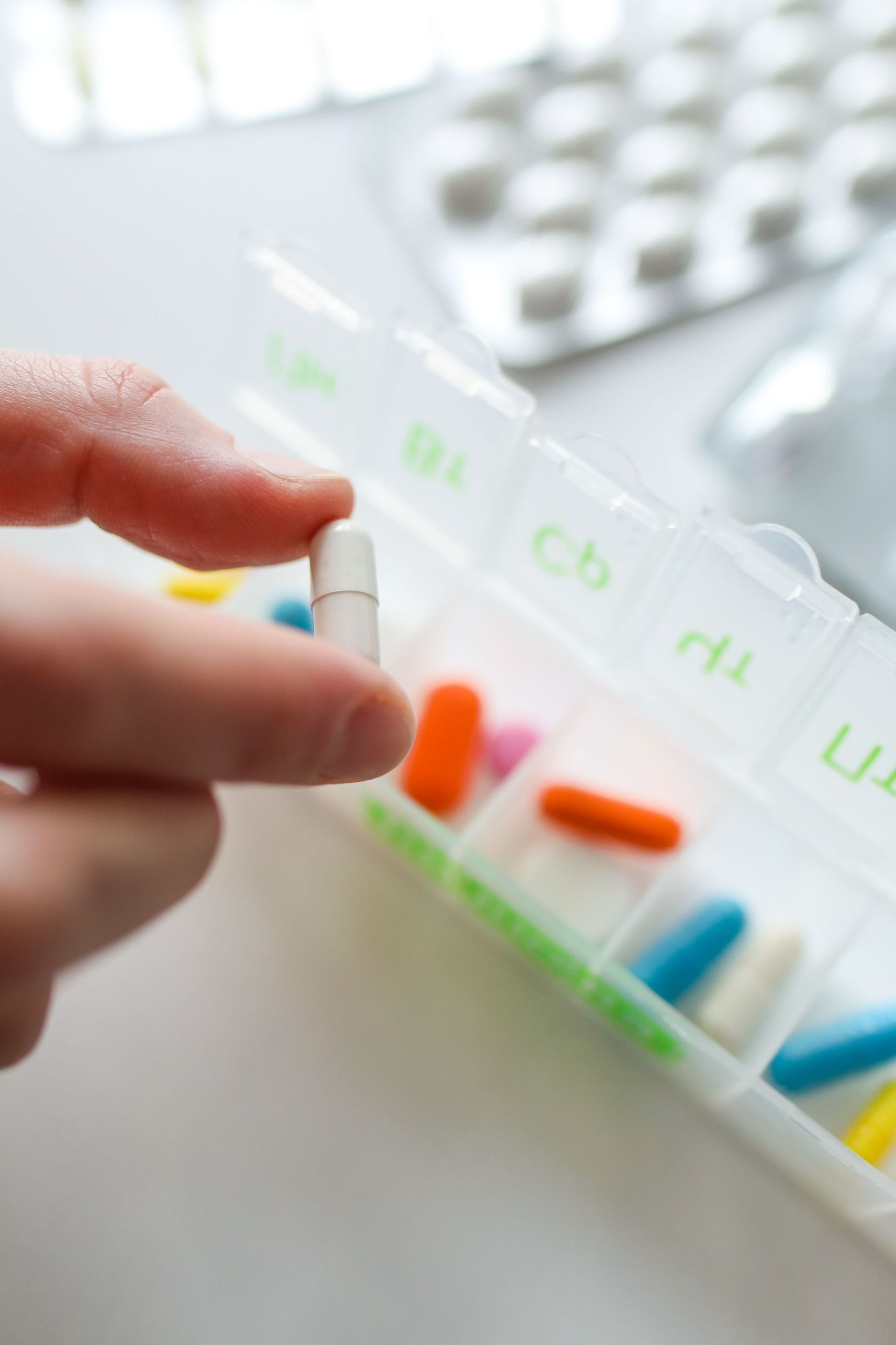 Hand placing a capsule into a weekly pill organizer with colored medication compartments