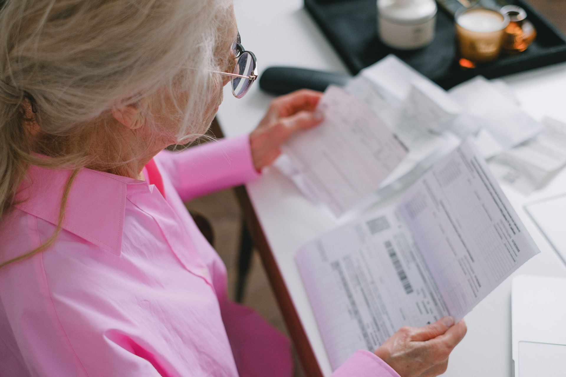 Woman in a pink shirt reviewing paperwork at a desk with a cup and candle nearby.