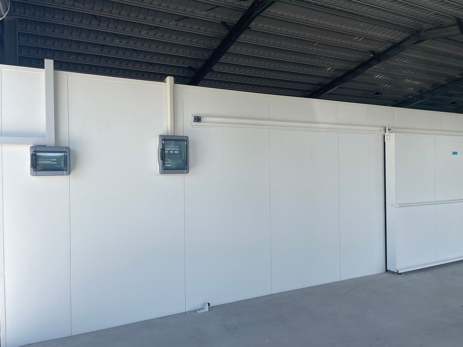 White Industrial Wall Under a Dark Roof With Two Mounted Electrical Boxes — Les Carman Cooling Solutions in El Arish, QLD