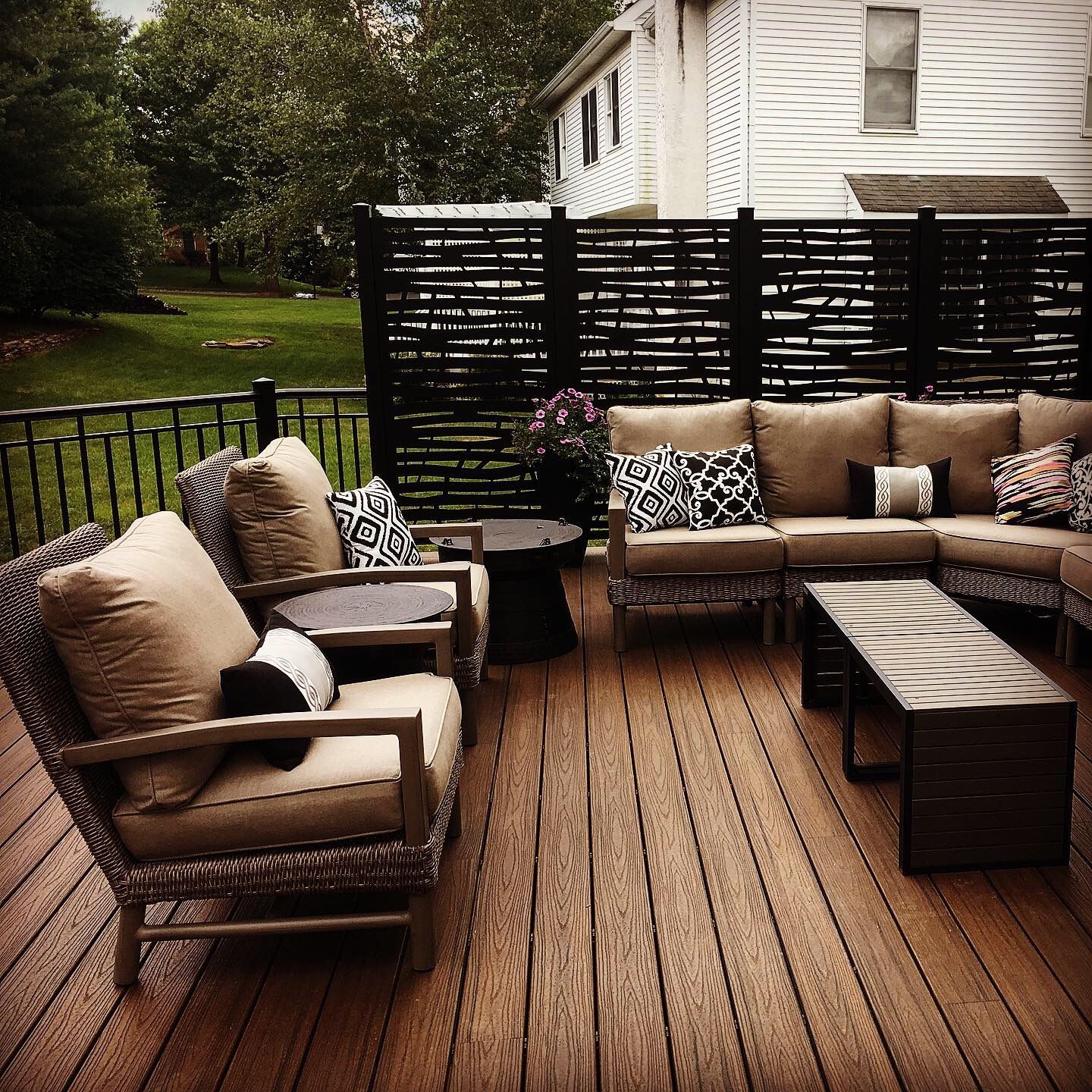 Patio with outdoor furniture, brown deck, black privacy screen, and white house background.