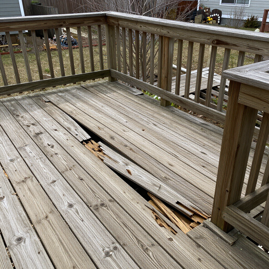 Weathered wooden deck with damaged, broken floorboards and railing, showing exposed wood beneath