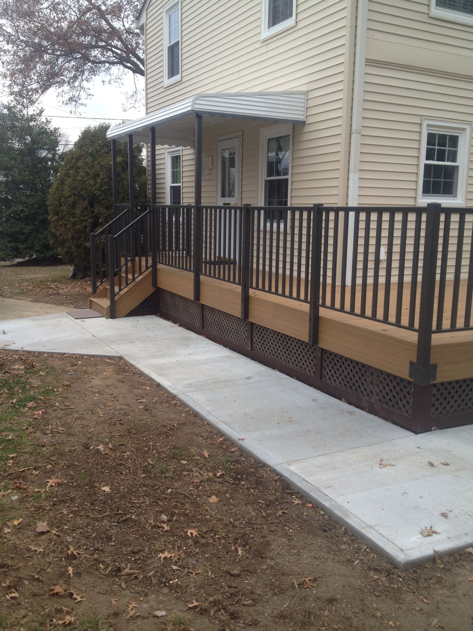 Newly constructed deck with railings, connected to a house with a concrete walkway.
