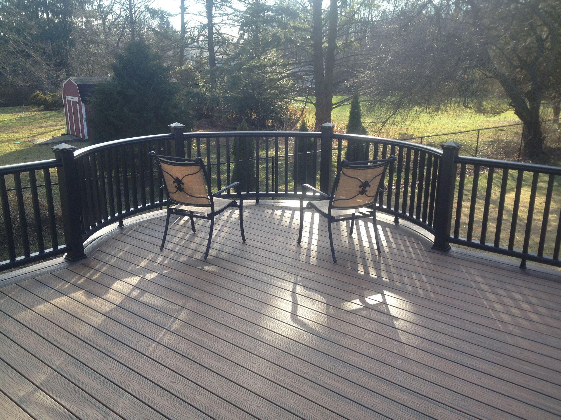 Deck with two chairs and small table, surrounded by a black railing, in a sunny backyard setting.