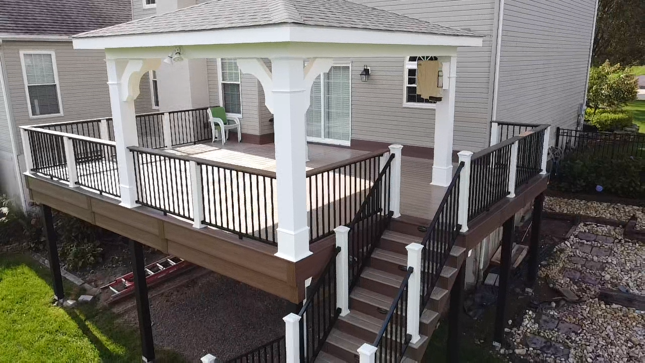 Two-story wooden deck with stairs and a white-columned pergola attached to a light gray house.
