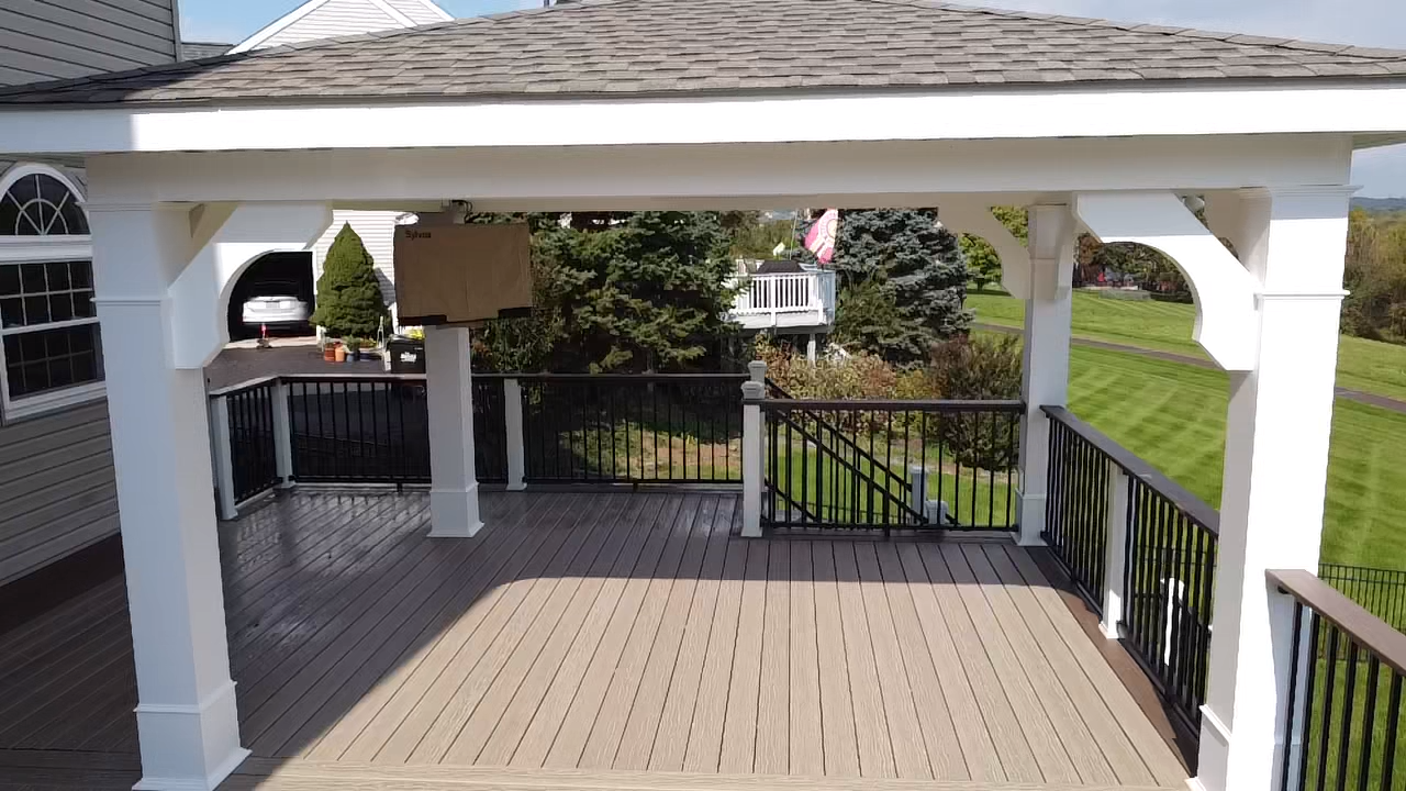 Wooden deck with white pergola, black railing, overlooking a green lawn with trees.
