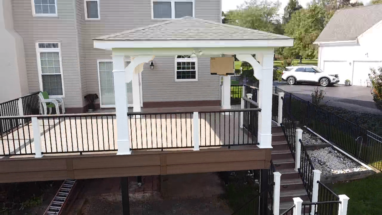Backyard deck with white gazebo, black railings, stairs, and a car in the driveway.