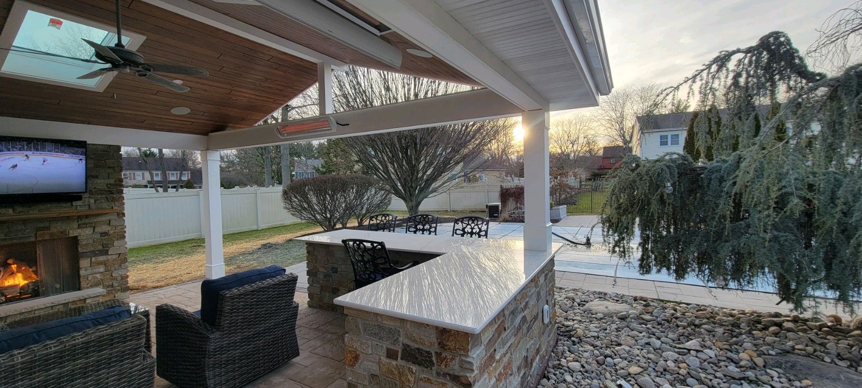 Outdoor kitchen with a bar, fireplace, and seating area. Overcast sky and bare trees.