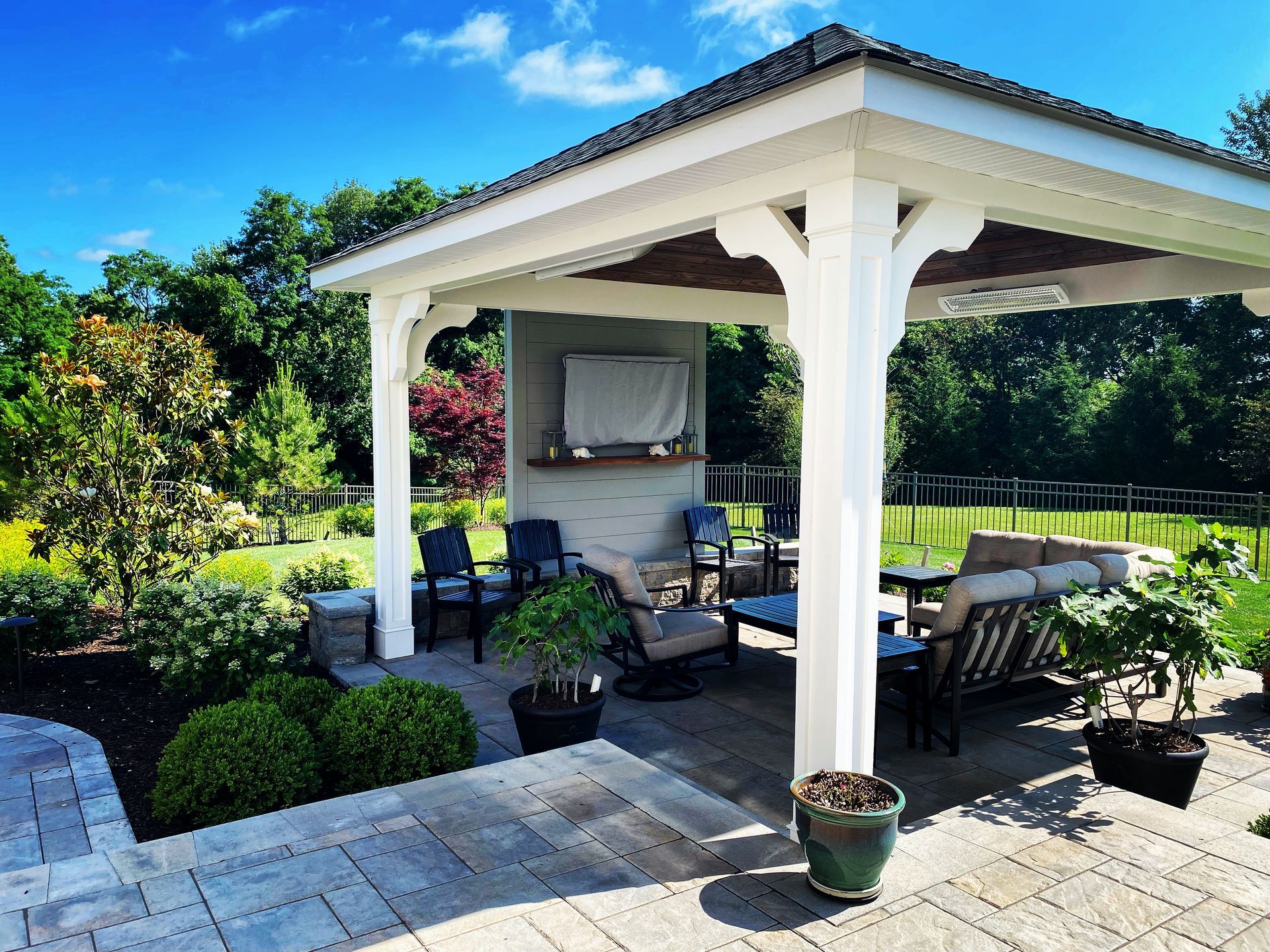 Patio with gazebo, seating area, television, and surrounding greenery under a blue sky.
