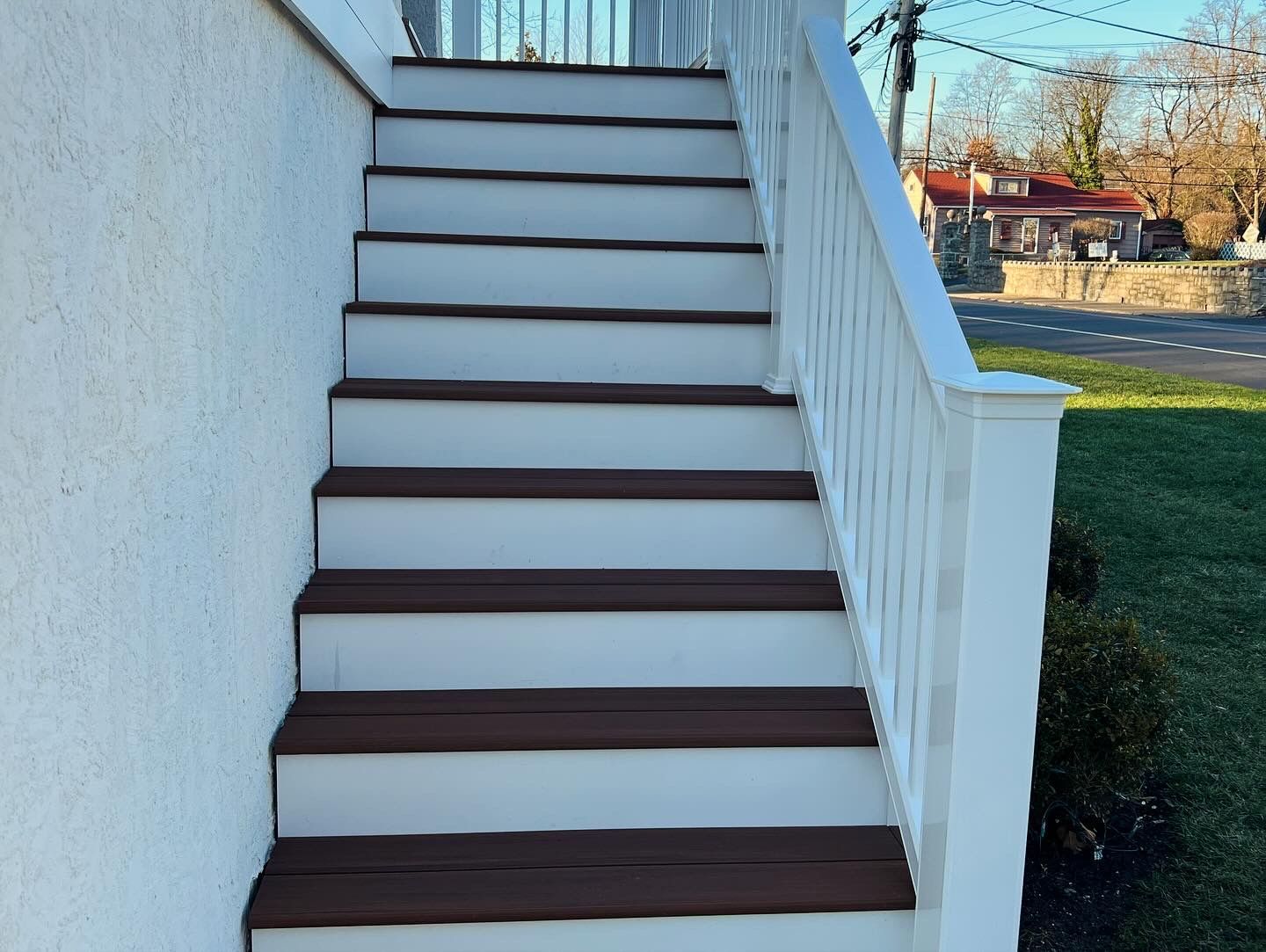 Outdoor staircase with white risers and brown treads, white railing, leading upwards.